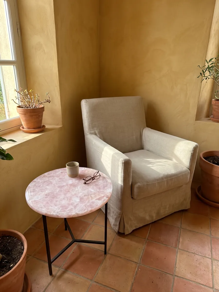 Side table with a rose quartz top next to an armchair: glassy pale pink with whiter fragments