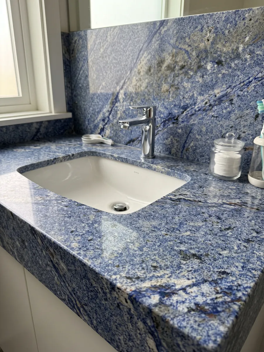 Vanity top and bathroom wall in Azul Bahia Granite with a white sink and chrome faucets: deep granular blue with white areas and dark patches