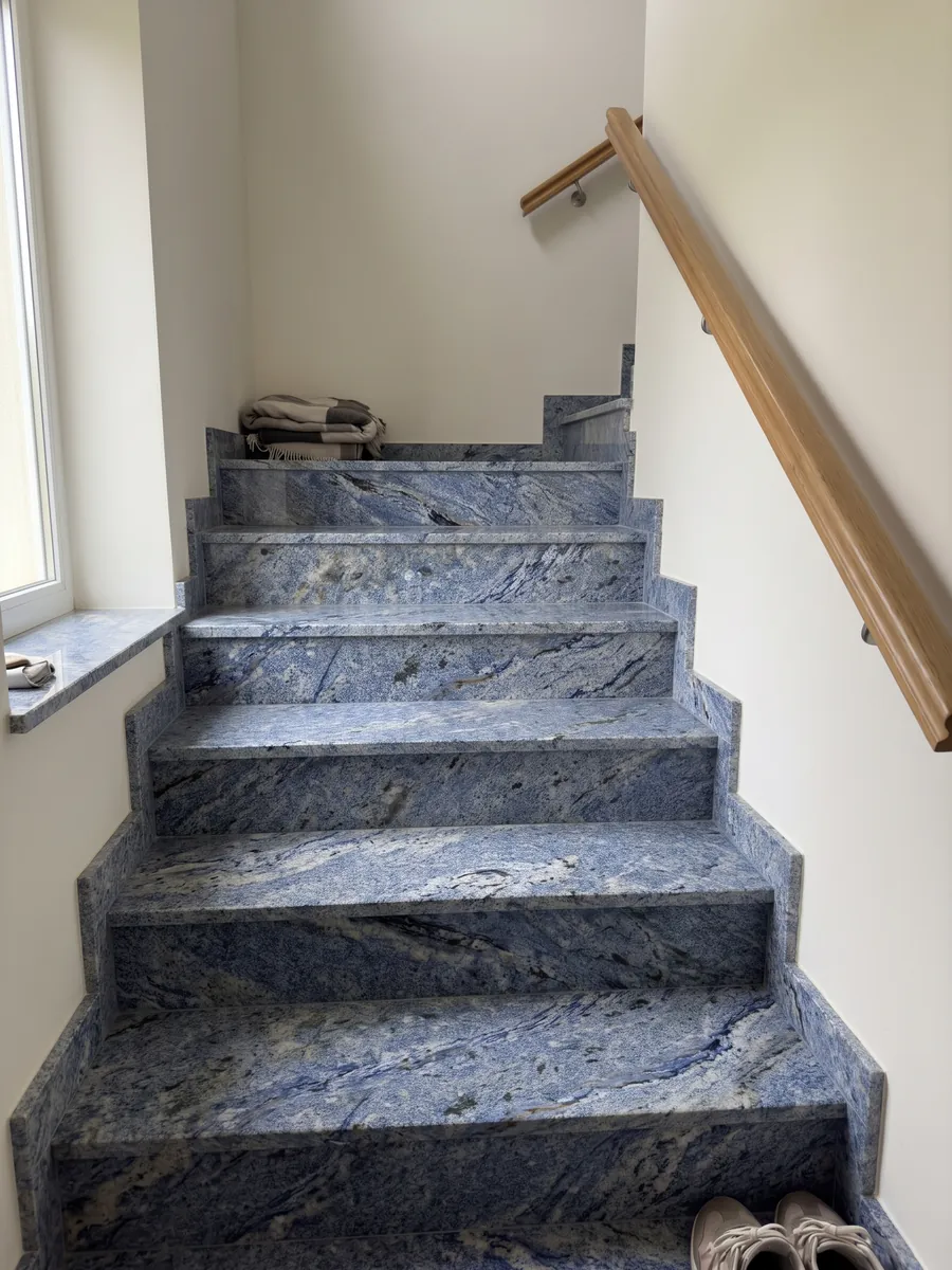 Interior staircase with Azul Bahia Granite treads and a handrail: deep granular blue with white areas and dark patches