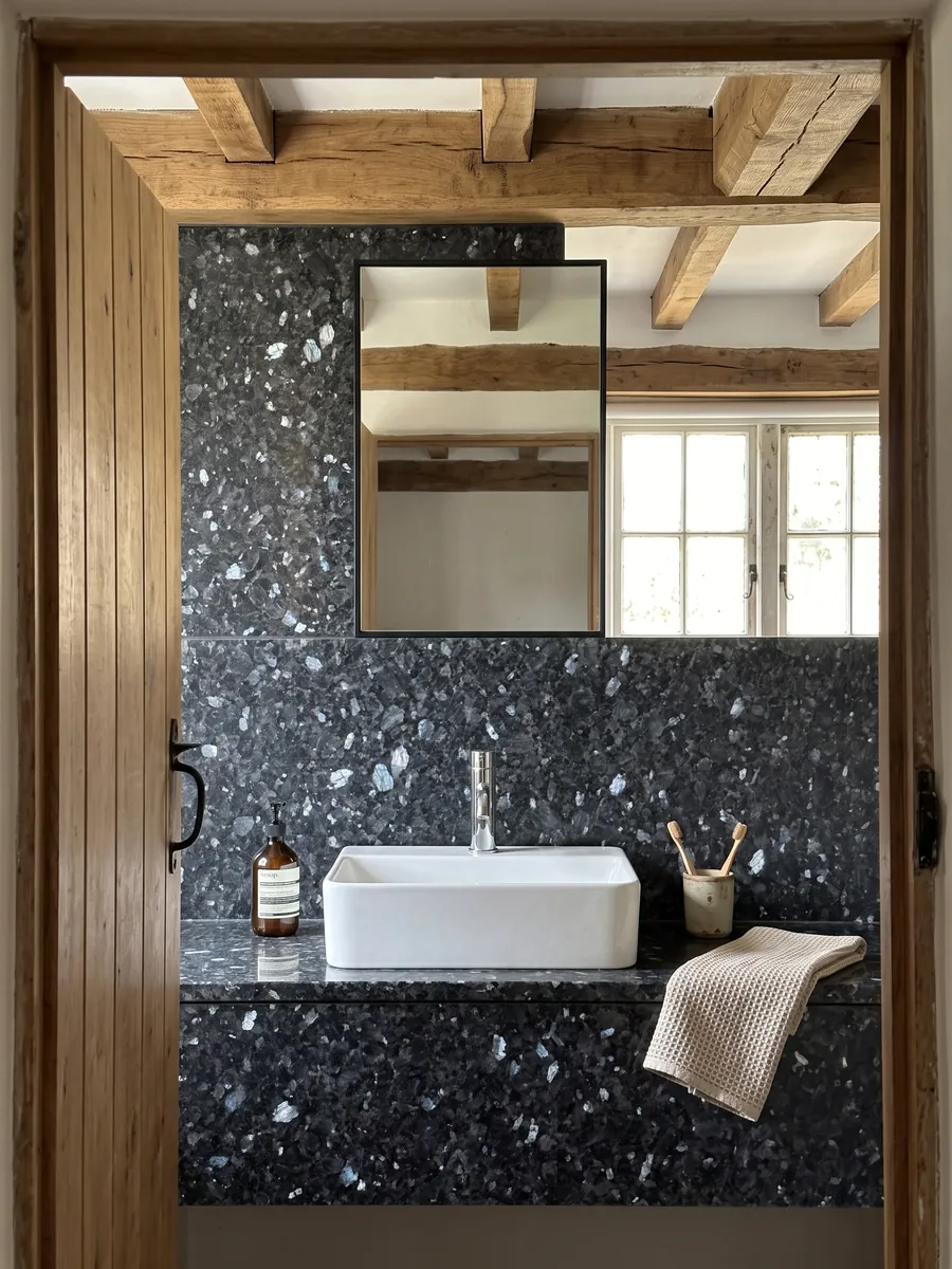 Bathroom vanity top and wall in Blue Pearl granite with a white sink and chrome faucets: near-black blue-gray with crystals that glint silvery blue