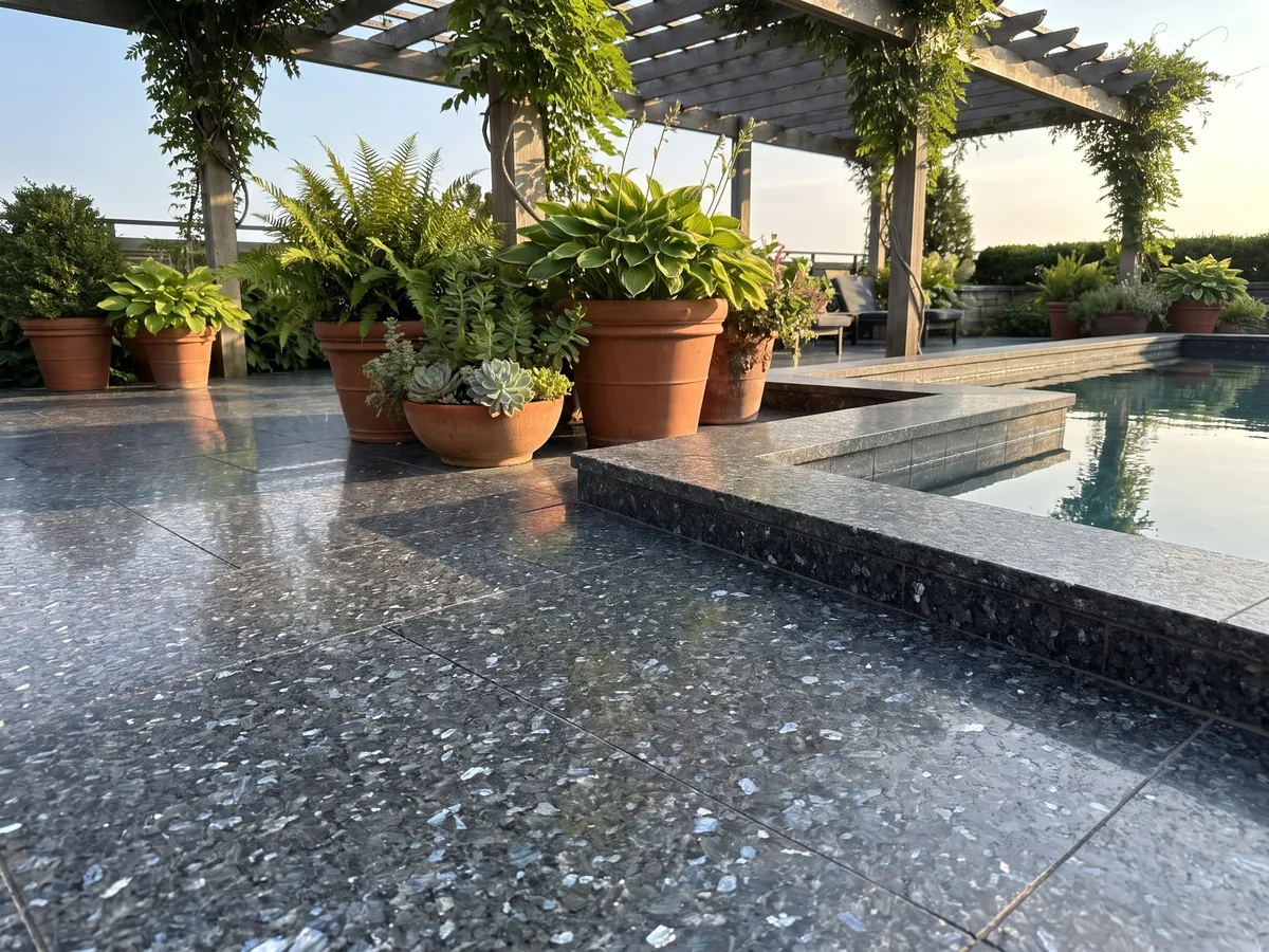 Terrace floor and pool coping in Blue Pearl granite with planters: near-black blue-gray with crystals that glint silvery blue