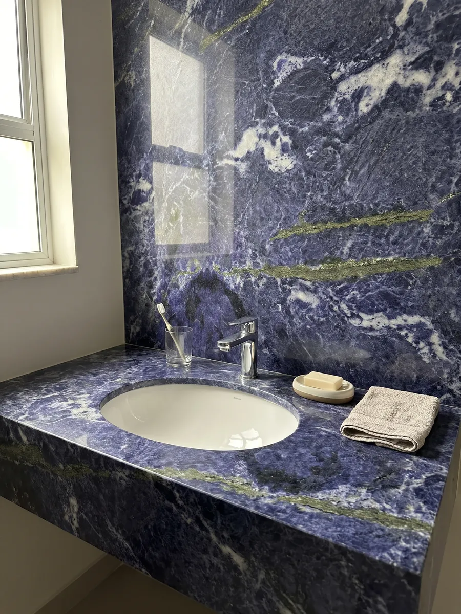 Bathroom vanity top and wall in Jeriba Blue granite with a white sink and chrome faucets: intense violet blue with white clouds and a golden green line