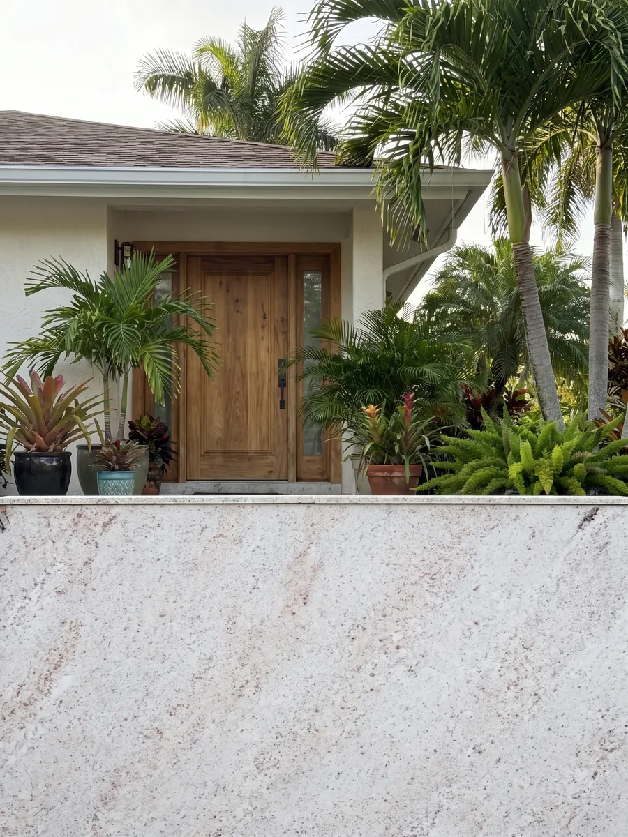 House facade clad in white Branco Siena granite next to a wood door: white with fine pink and gray speckling