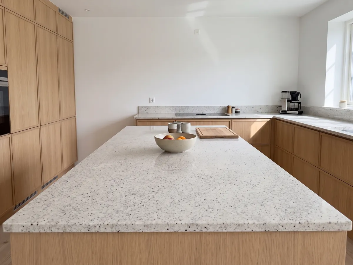 Kitchen island with a Blanco Dallas granite countertop and a straight edge in a kitchen with natural light: creamy white with fine gray speckling and small burgundy dots