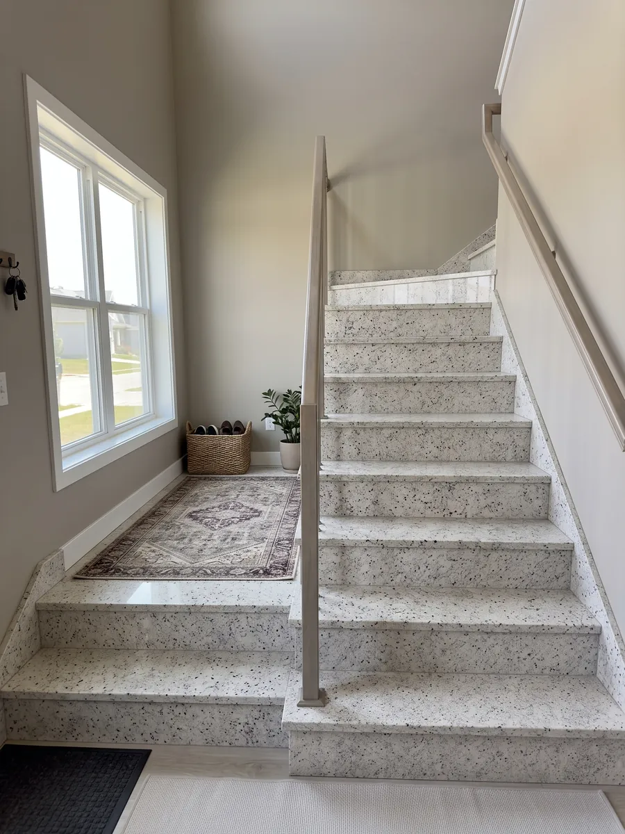 Interior staircase with Blanco Dallas granite steps and a handrail: creamy white with fine gray speckling and small burgundy dots