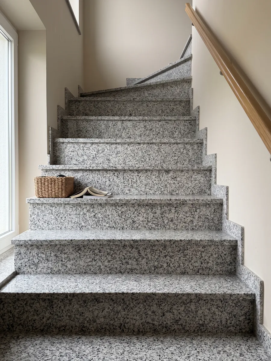 Interior staircase with white Bianco Sardo granite steps and a handrail: coarse-grained white with gray and black crystals