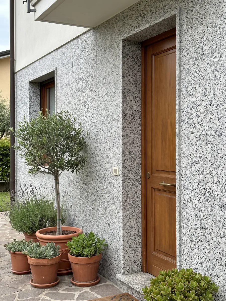 House facade clad in white Bianco Sardo granite next to a wood door: coarse-grained white with gray and black crystals