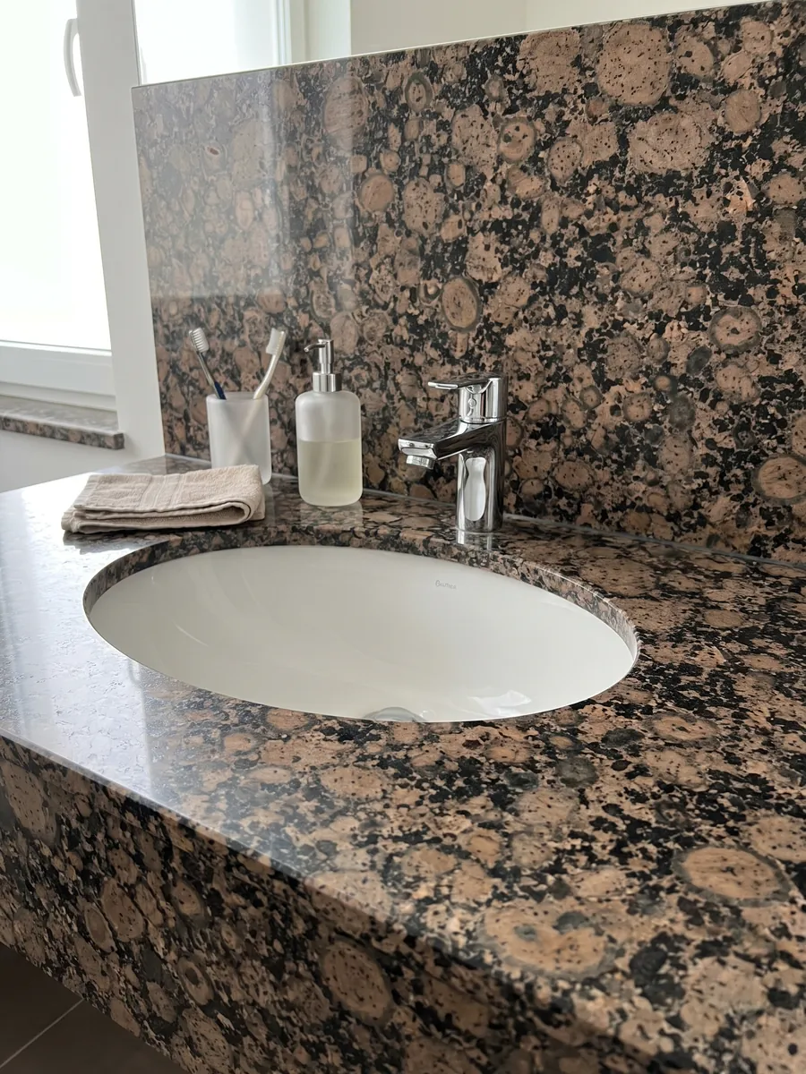 Vanity top and bathroom wall in Baltic Brown granite with a white sink and chrome faucets: round brown grains with rings over a speckled black background