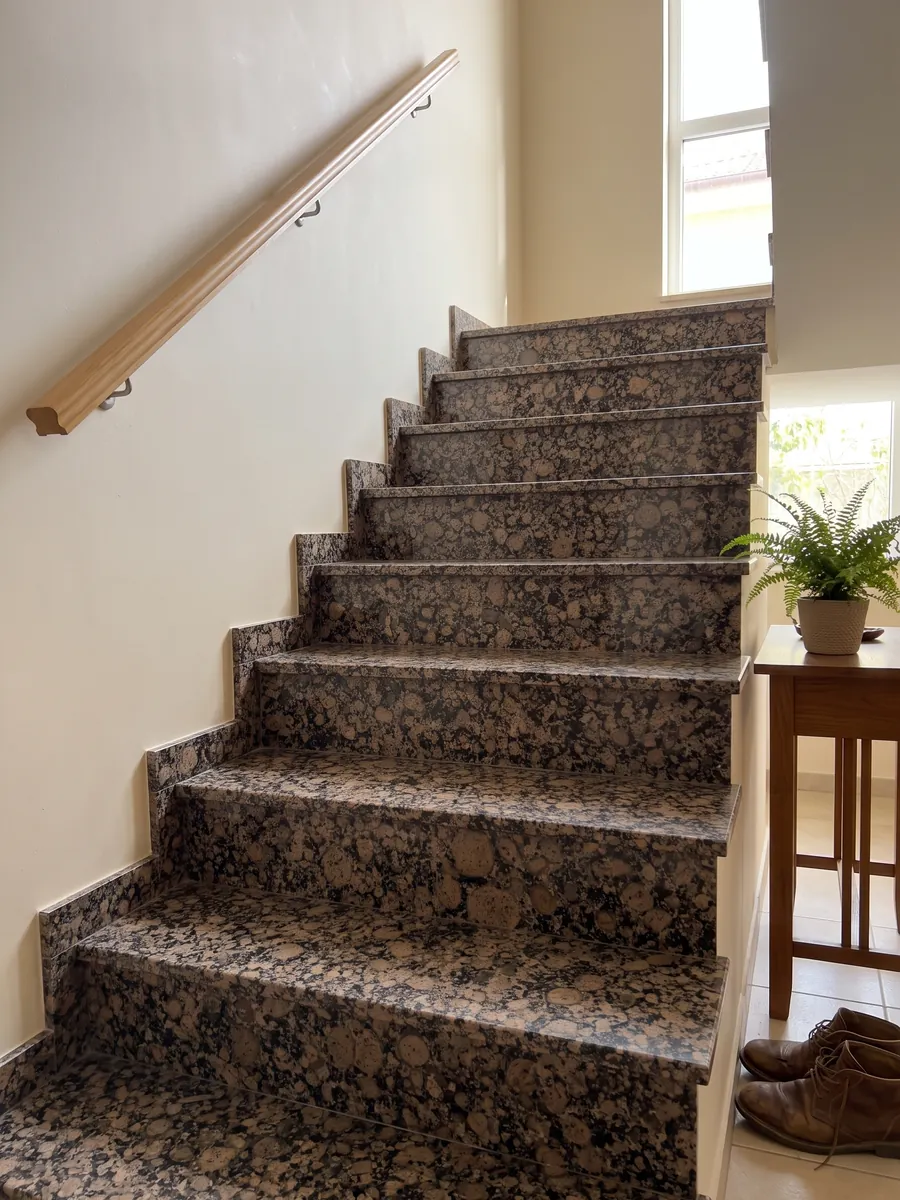 Interior staircase with Baltic Brown granite steps and a handrail: round brown grains with rings over a speckled black background