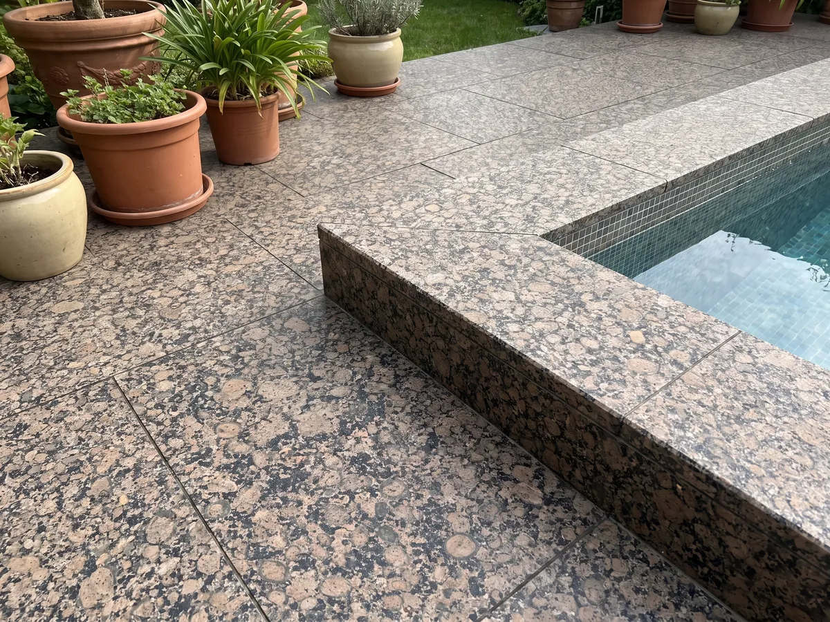 Terrace floor and pool edge in Baltic Brown granite with planters: round brown ringed grains on a black speckled background