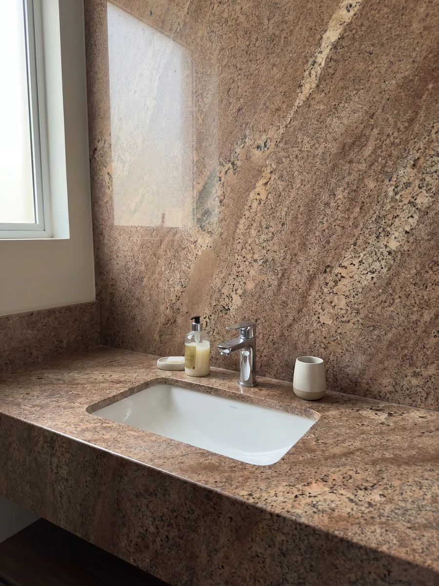 Bathroom vanity top and wall in Juparana Florence granite with a white sink and chrome faucets: grainy coppery brown with diffuse beige areas