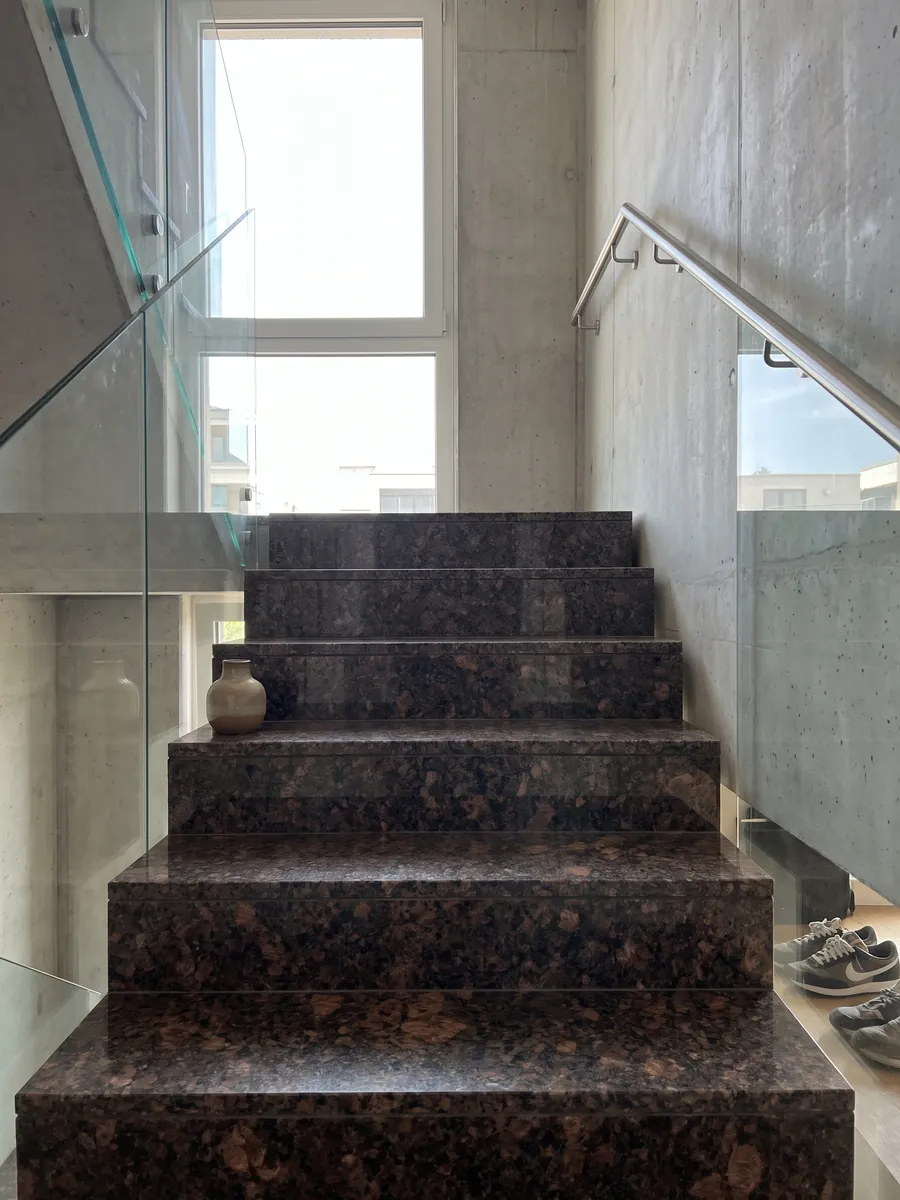 Interior staircase with Tan Brown granite steps and a handrail: chocolate brown with large copper patches and black dots