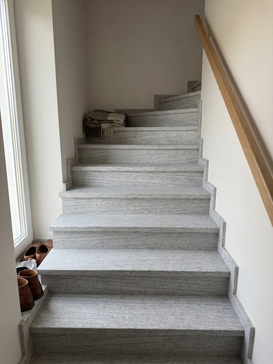 Interior staircase with gray Beola Bianca granite steps and a handrail: light gray with fine horizontal striping and small glints