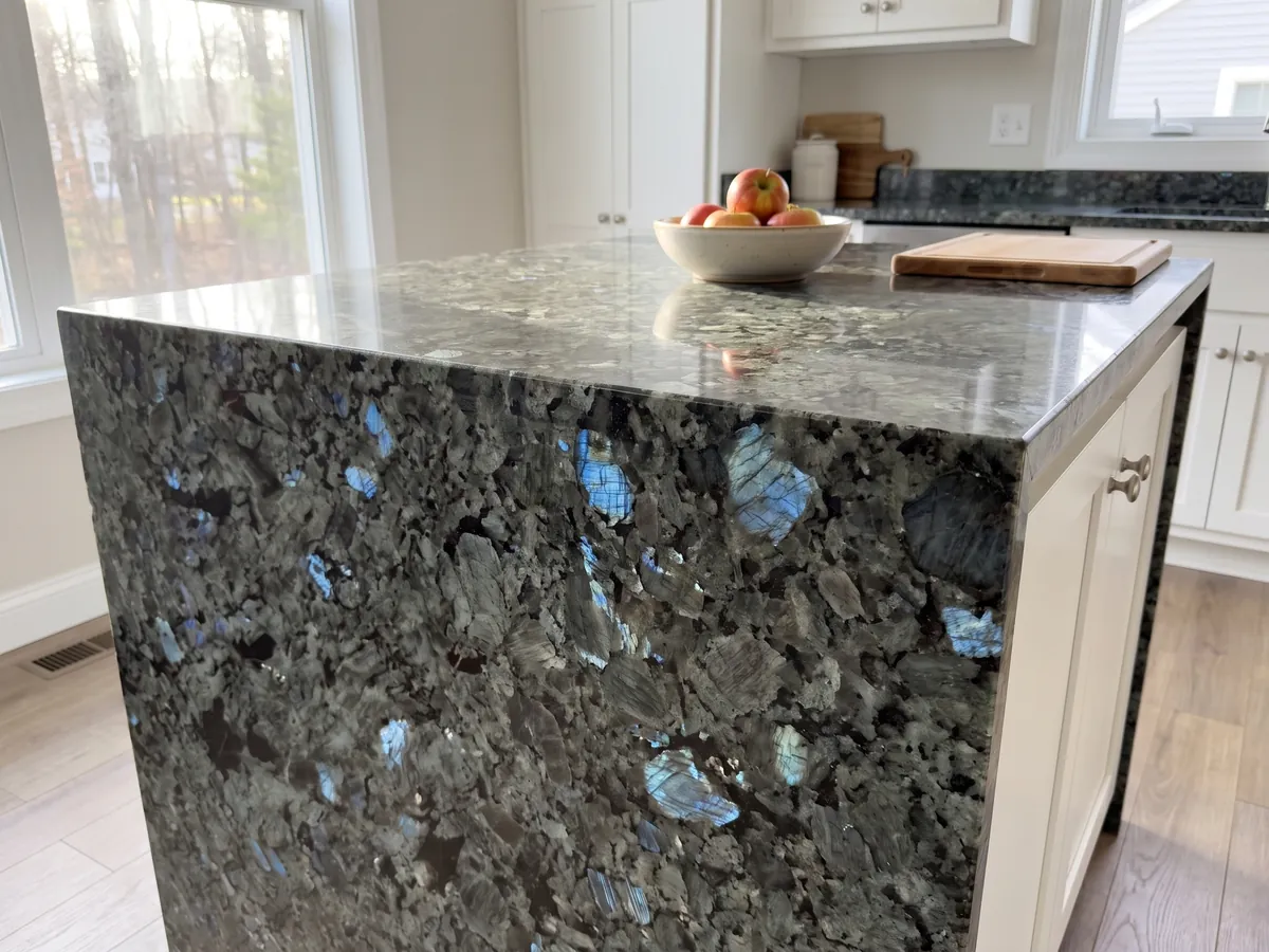 Kitchen island with a Labradorite granite countertop and a straight edge in a kitchen with natural light: large greenish gray crystals with iridescent blue flashes