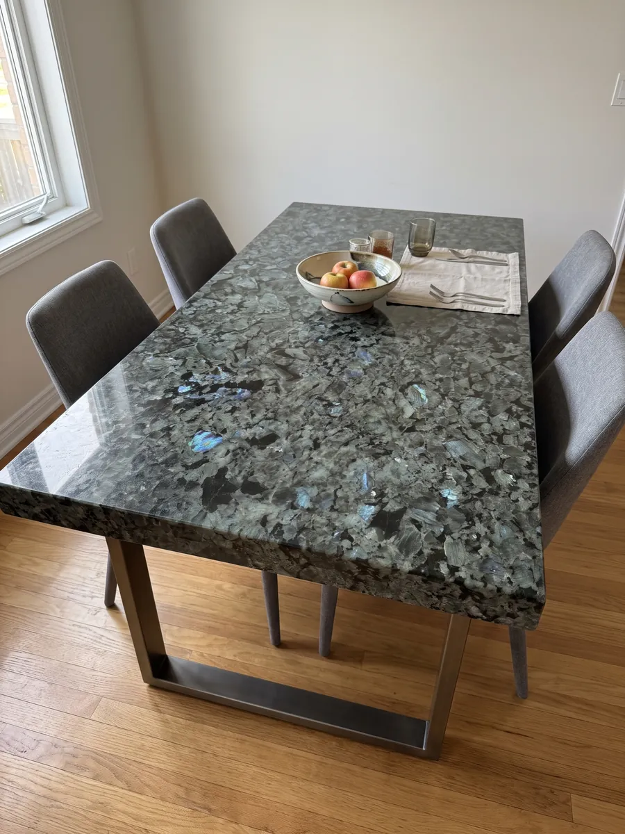 Dining table with a Labradorite granite top on a steel base: large greenish-gray crystals with iridescent blue flashes
