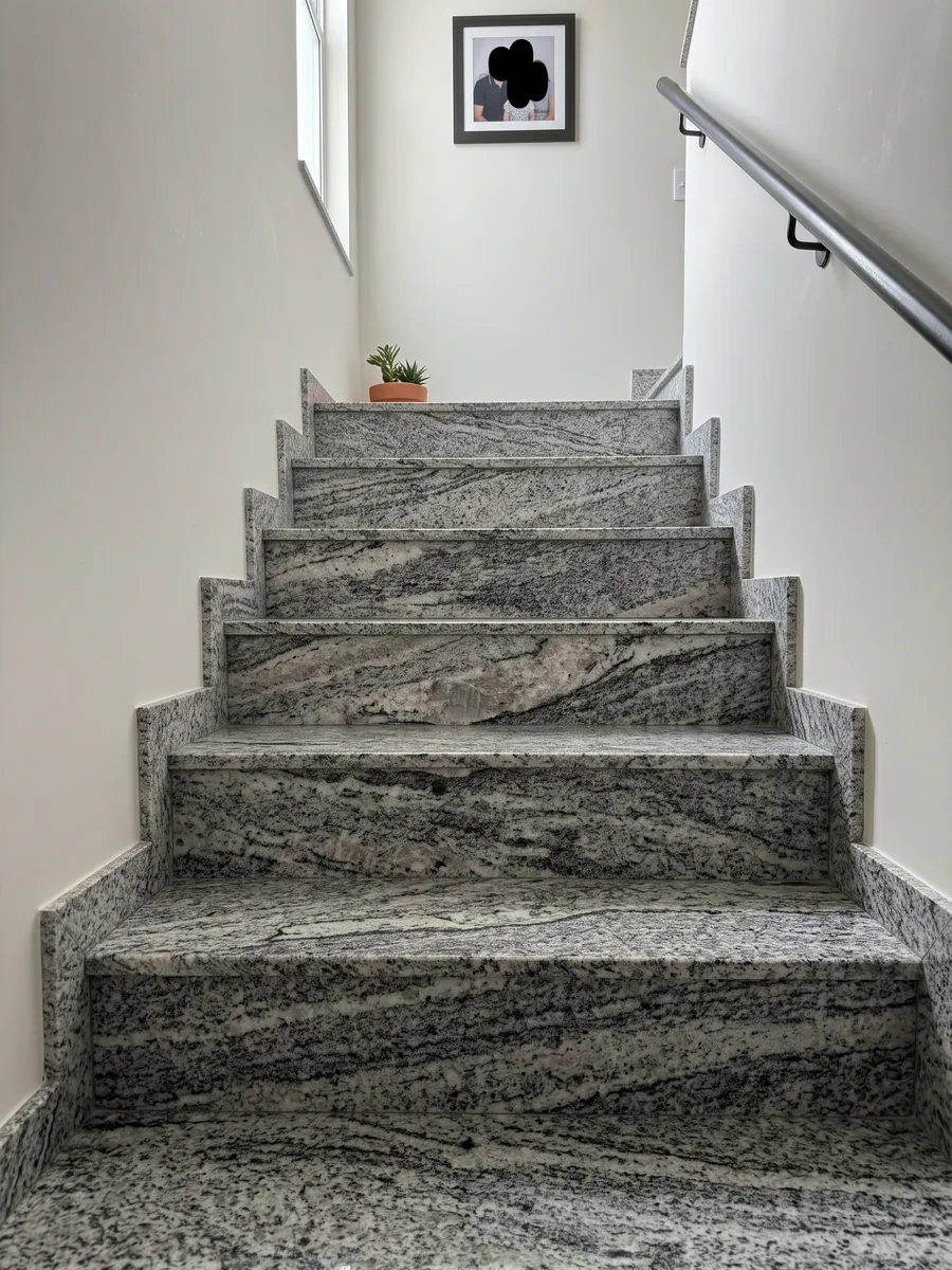 Indoor staircase with Piracema White gray granite steps and a handrail: wavy gray and white bands with one large light fragment