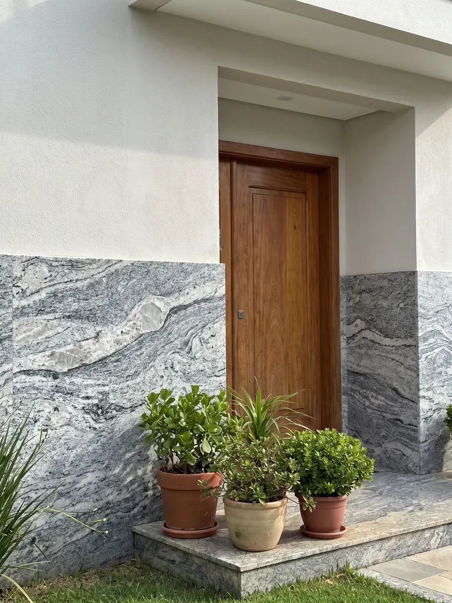 House facade clad in Piracema White gray granite next to a wood door: wavy gray and white bands with one large light fragment