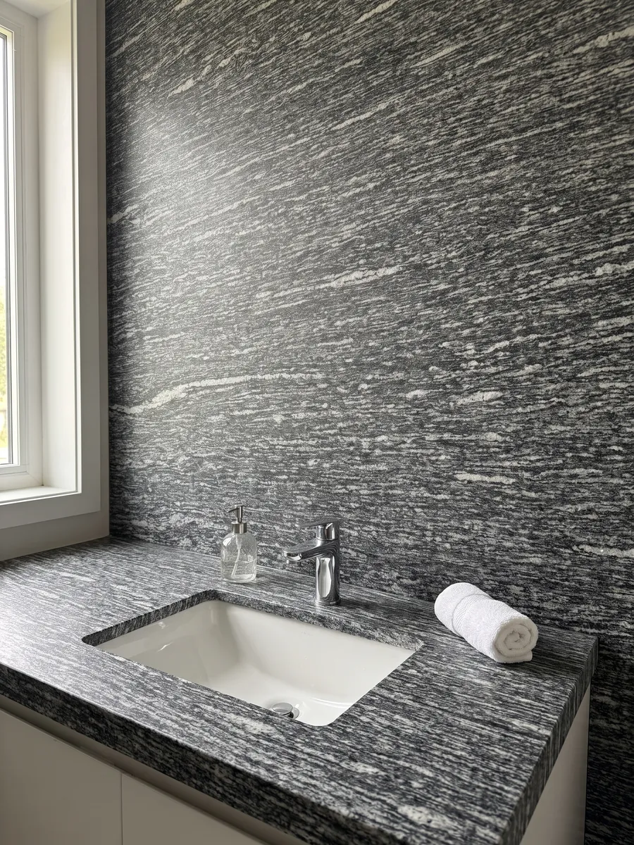 Vanity top and bathroom wall in Serizzo granite with a white sink and chrome faucets: dark gray with elongated horizontal white streaks