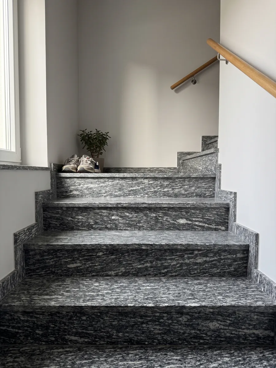 Interior staircase with Serizzo granite steps and a handrail: dark gray with elongated horizontal white streaks