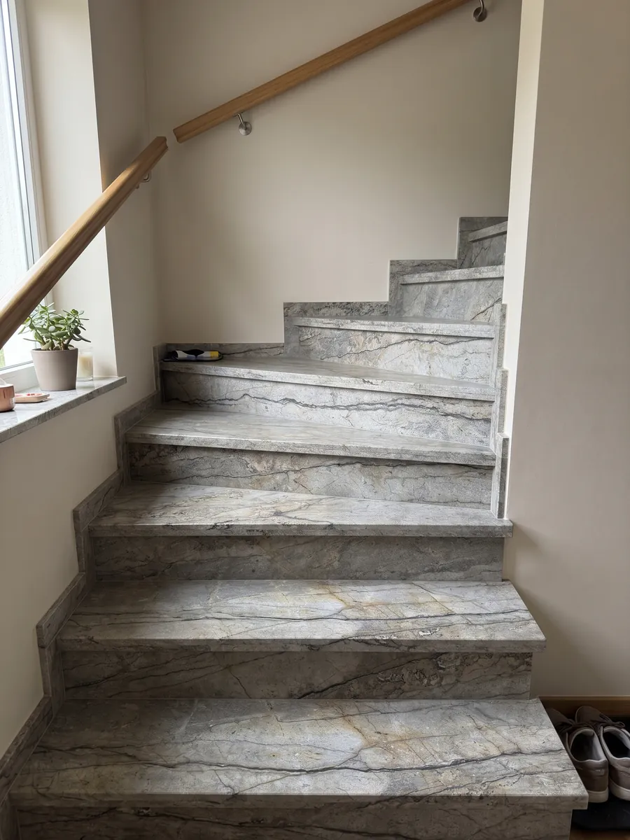 Interior staircase with Silver Roots granite steps and a handrail: taupe gray with horizontal dark veins and a natural stone look
