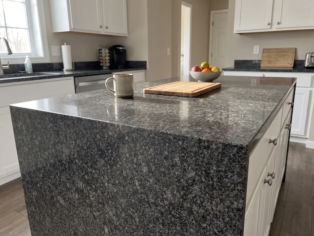 Kitchen island with a Steel Grey granite countertop and a straight edge in a kitchen with natural light: medium steel gray grain over a near-black background, with small lighter gray areas spread throughout