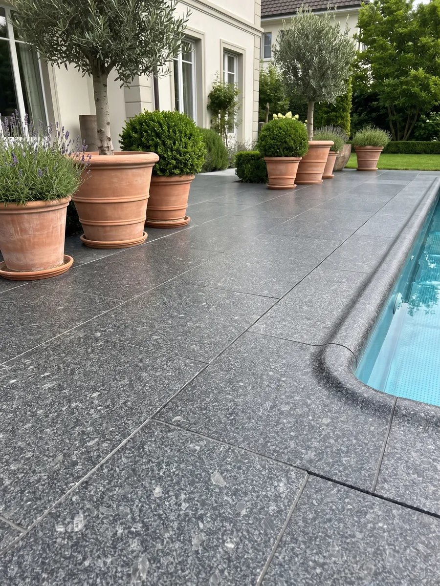 Terrace floor and pool edge in Steel Grey granite with planters: medium steel-gray grain on an almost black background, with small lighter gray areas spread throughout