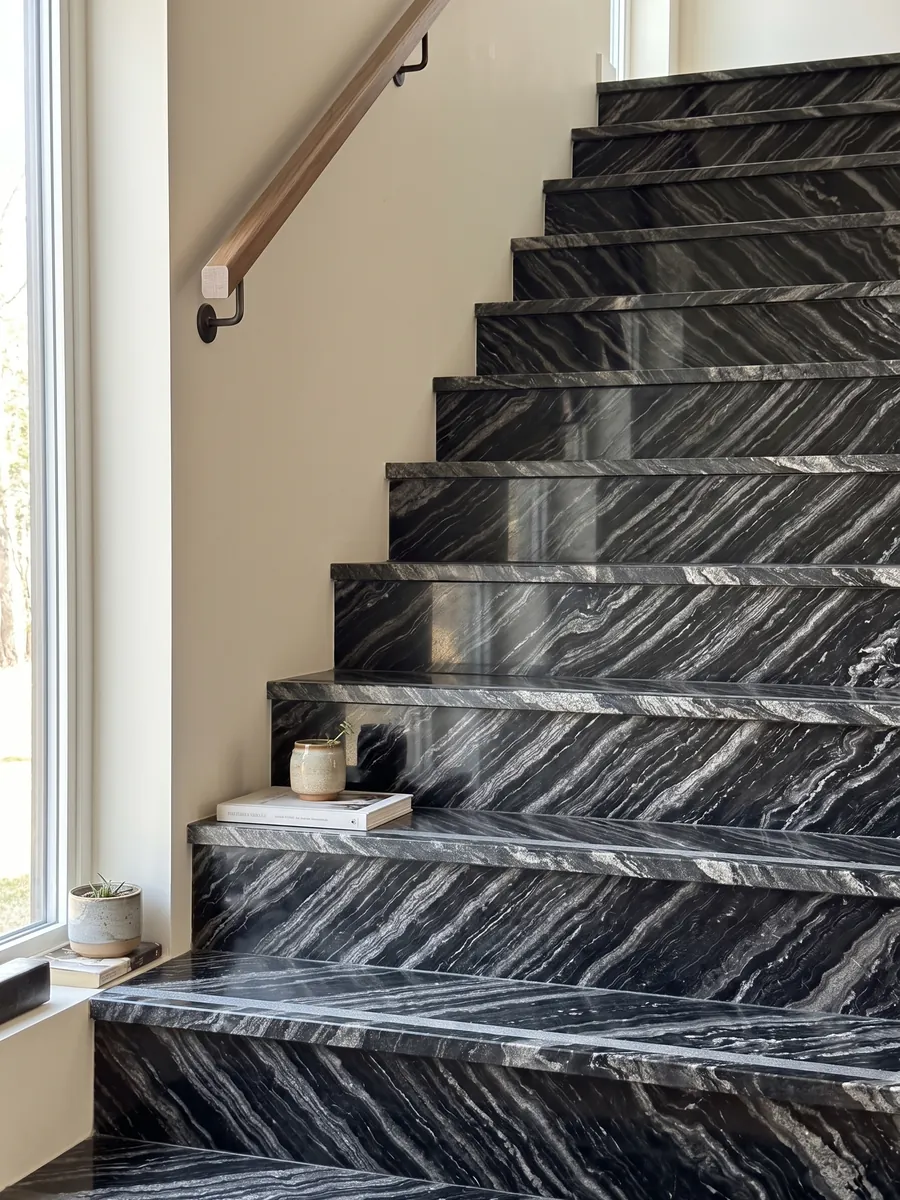Interior staircase with black Agata Black granite treads and a handrail: black with parallel wavy silver-gray bands set on the diagonal