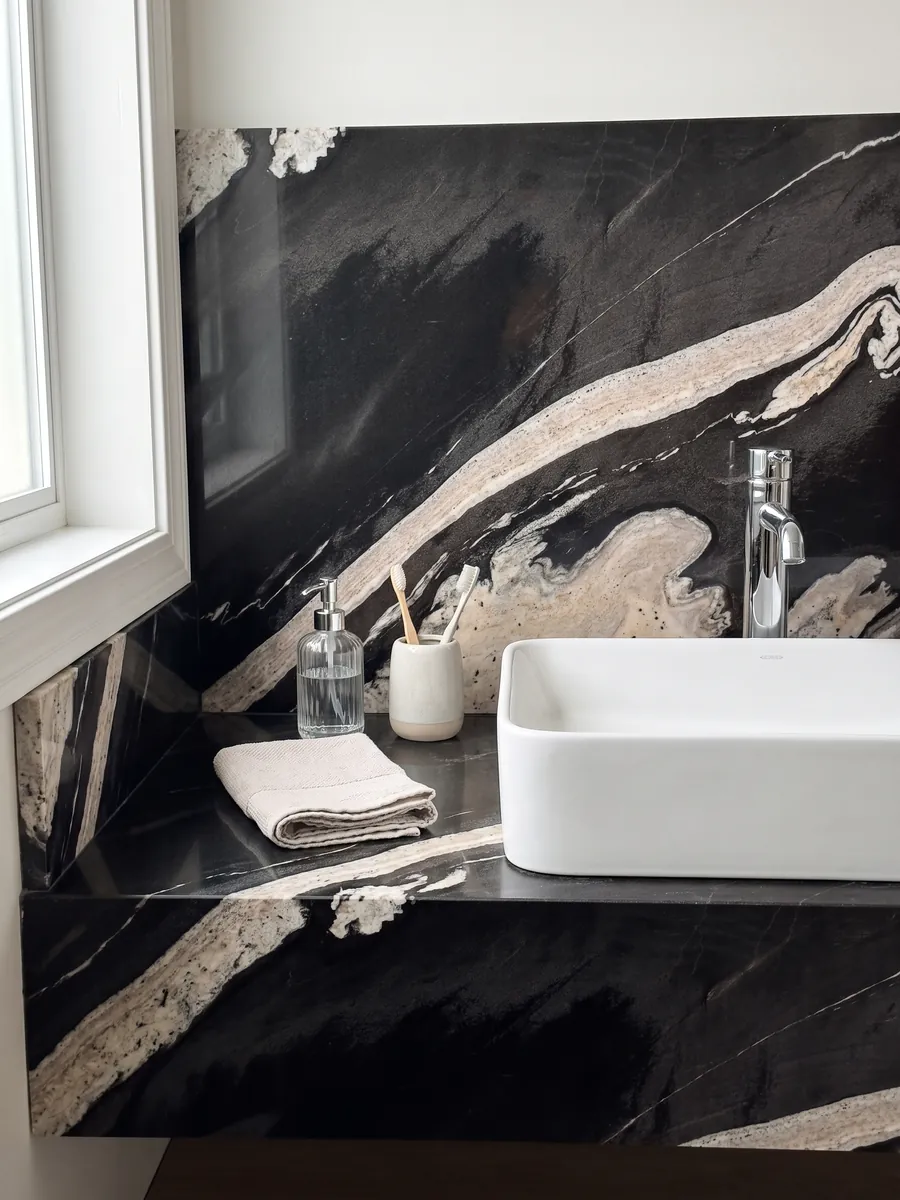 Vanity top and bathroom wall in black Copacabana granite with a white sink and chrome faucets: black with a wavy cream band crossing on the diagonal