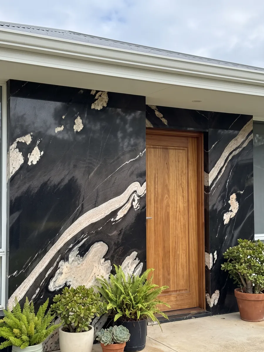 House facade clad in black Copacabana granite next to a wood door: black with a wavy cream band crossing on the diagonal