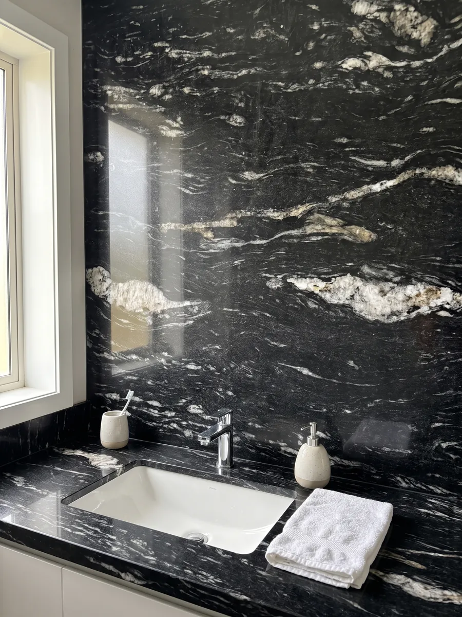 Vanity top and bathroom wall in Cosmic Black granite with a white sink and chrome faucets: black with horizontal wavy white veining