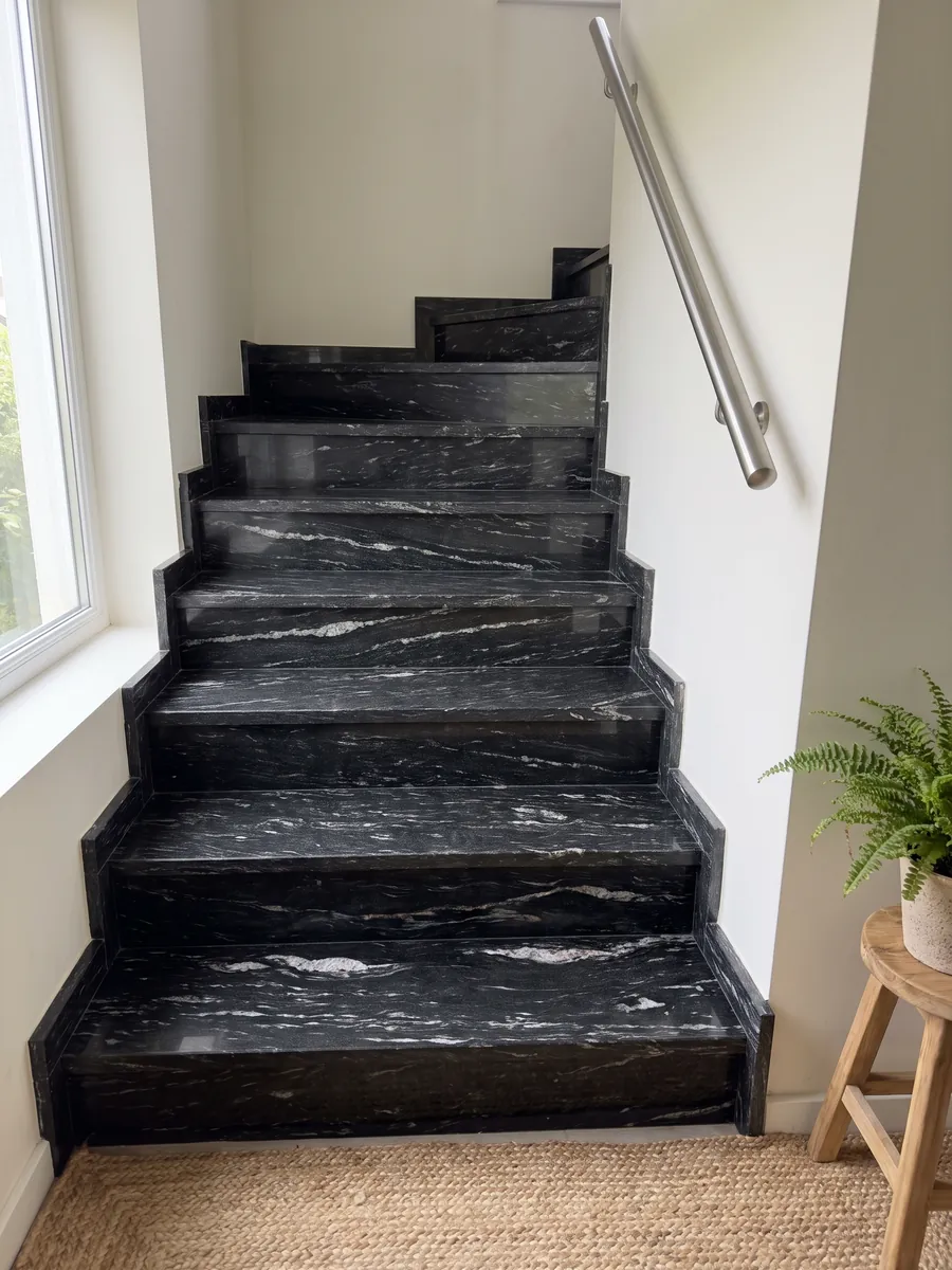 Interior staircase with Cosmic Black granite steps and a handrail: black with horizontal wavy white veining