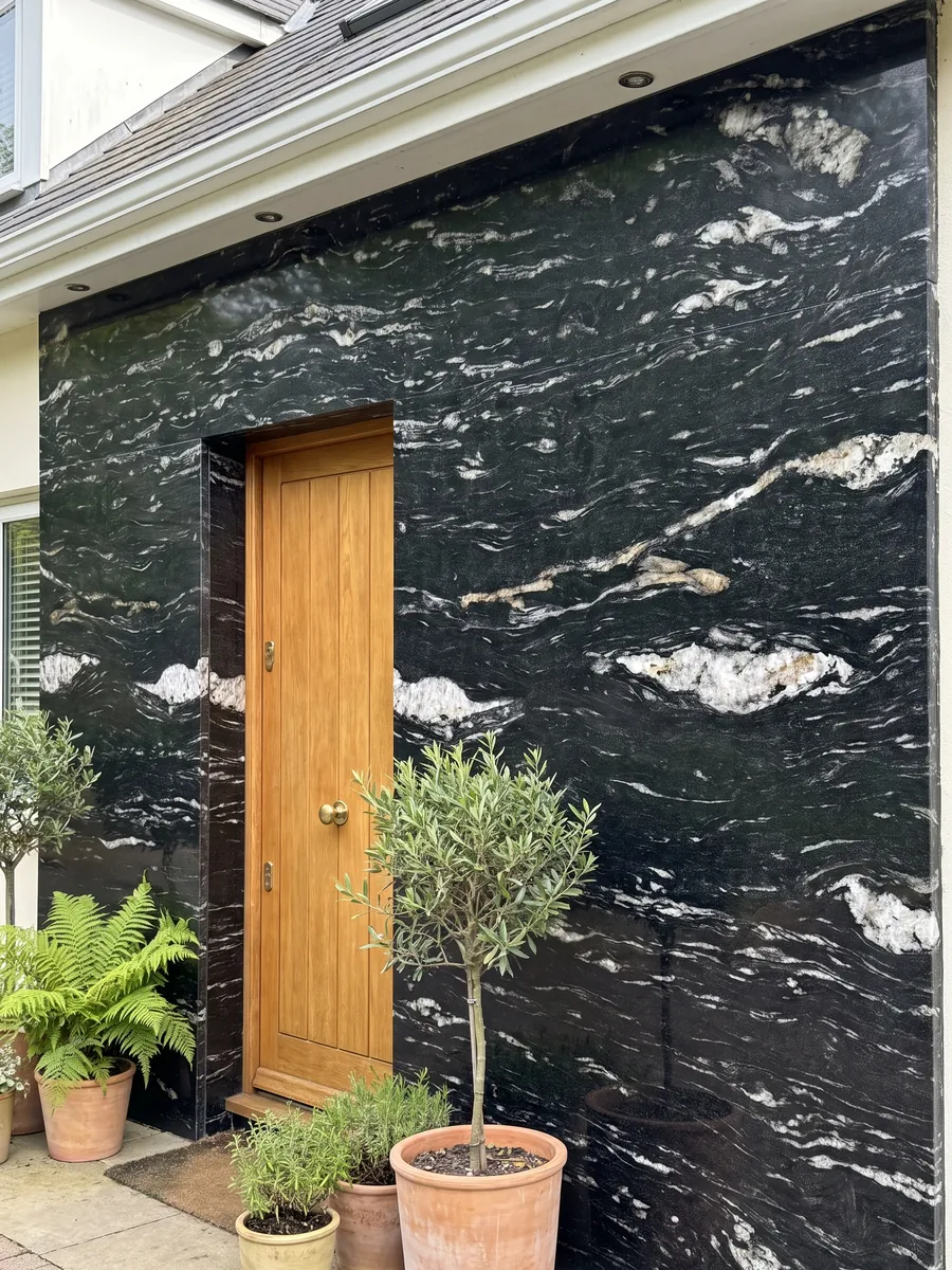 House facade clad in Cosmic Black granite beside a wood door: black with horizontal wavy white veining