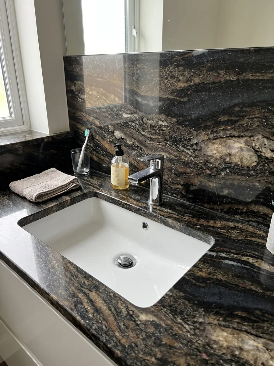 Vanity top and bathroom wall in Cosmic Gold granite with a white sink and chrome faucets: black with golden and bronze patches in horizontal waves