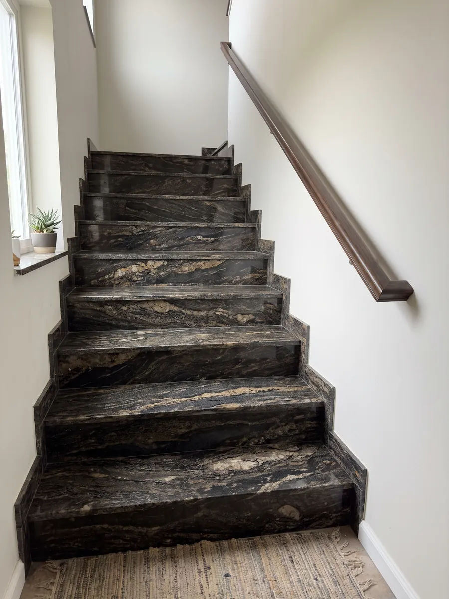 Interior staircase with Cosmic Gold granite steps and a handrail: black with golden and bronze patches in horizontal waves