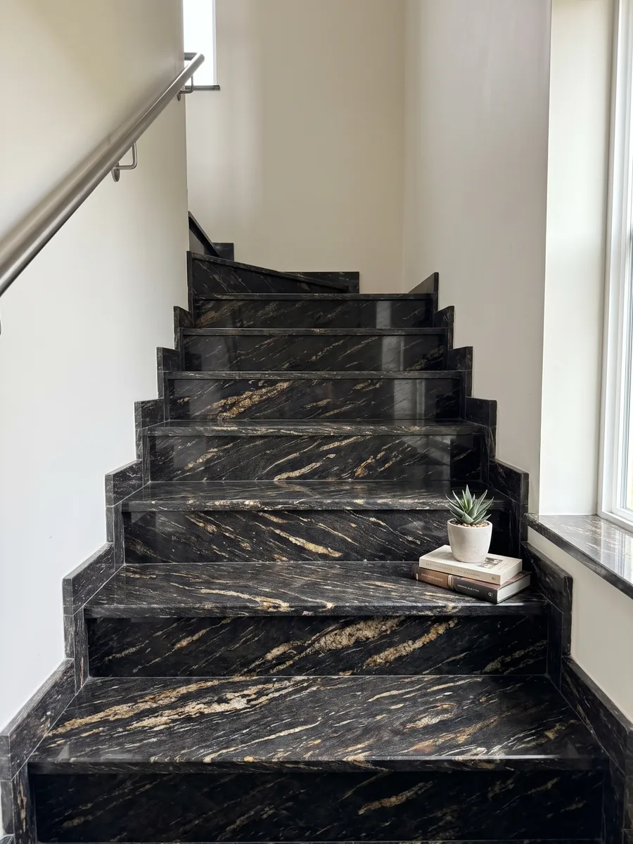 Indoor staircase with black Matrix granite steps and a handrail: black with elongated golden streaks on the diagonal