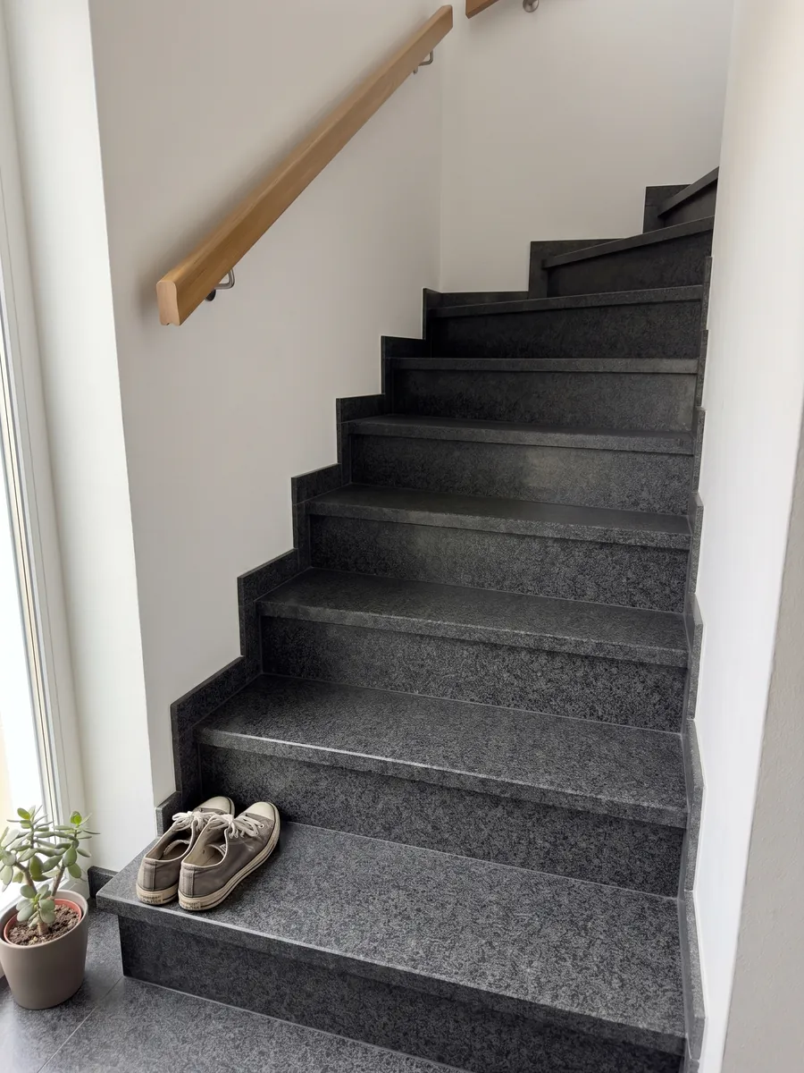 Indoor staircase with Nero Africa black granite steps and a handrail: uniform fine-grained black with a light gray speckle