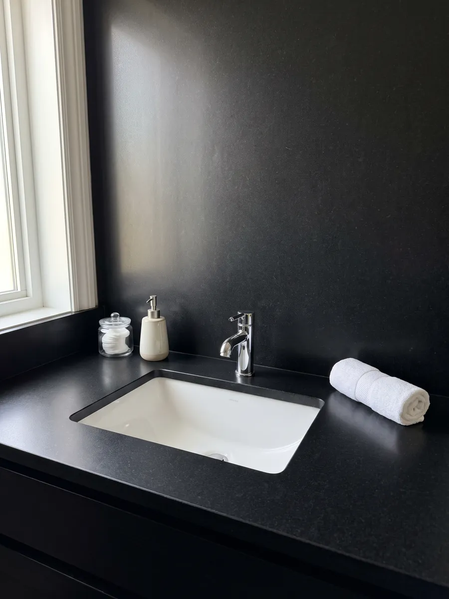 Bathroom vanity top and wall in Nero Assoluto black granite with a white sink and chrome faucets: uniform black with no pattern