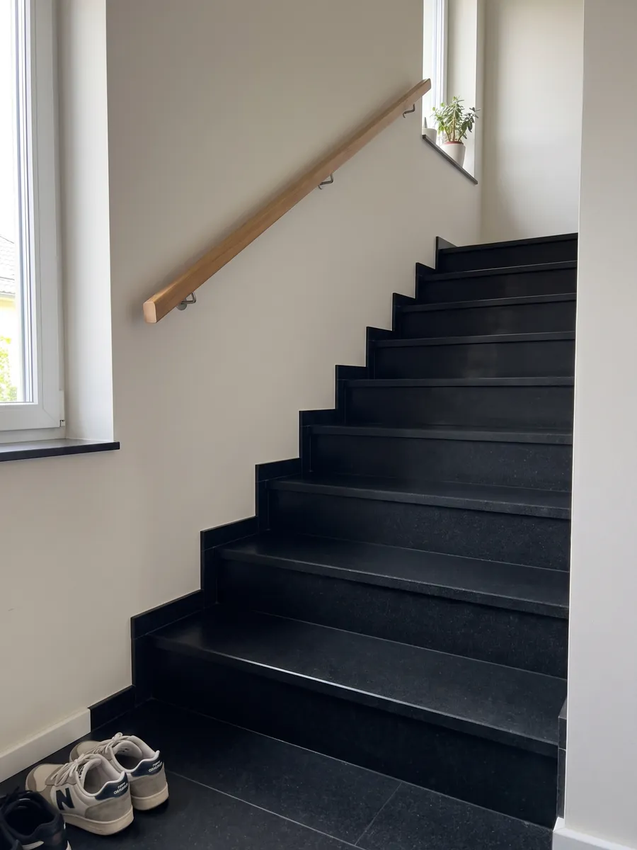 Indoor staircase with Nero Assoluto black granite steps and a handrail: uniform black with no pattern