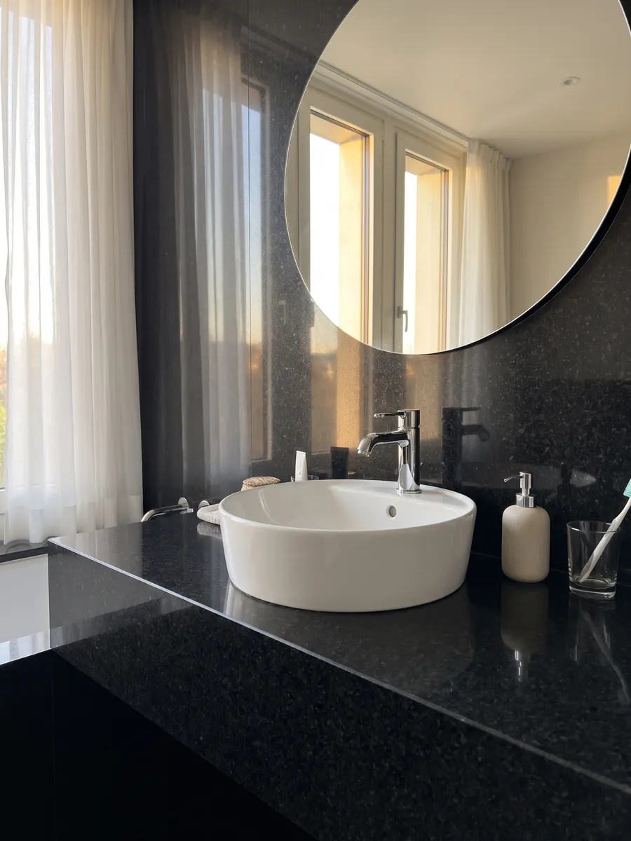 Bathroom vanity top and wall in Negro San Gabriel granite with a white sink and chrome fixtures: deep black with a medium grain and dark gray specks that show up close