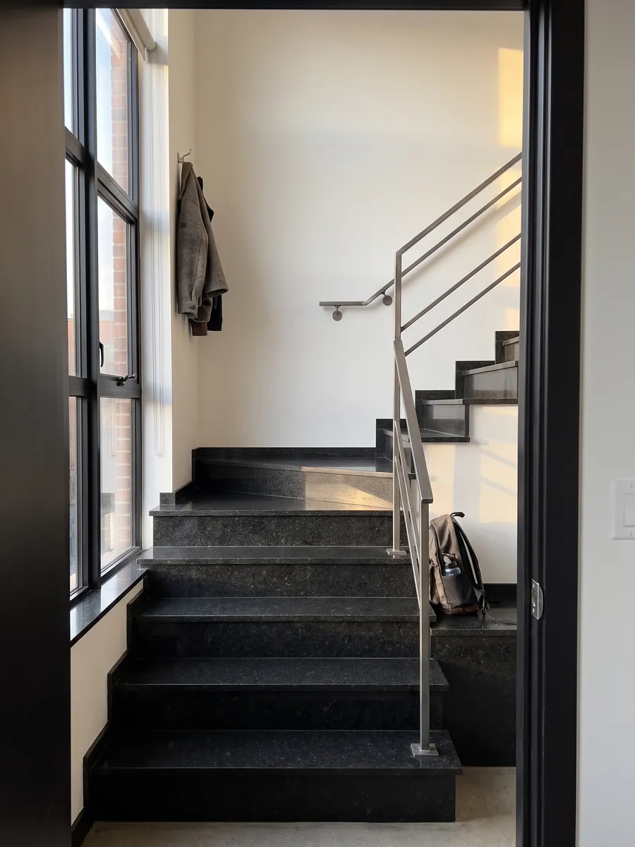 Indoor staircase with Negro San Gabriel granite steps and a handrail: deep black with a medium grain and dark gray specks that show up close