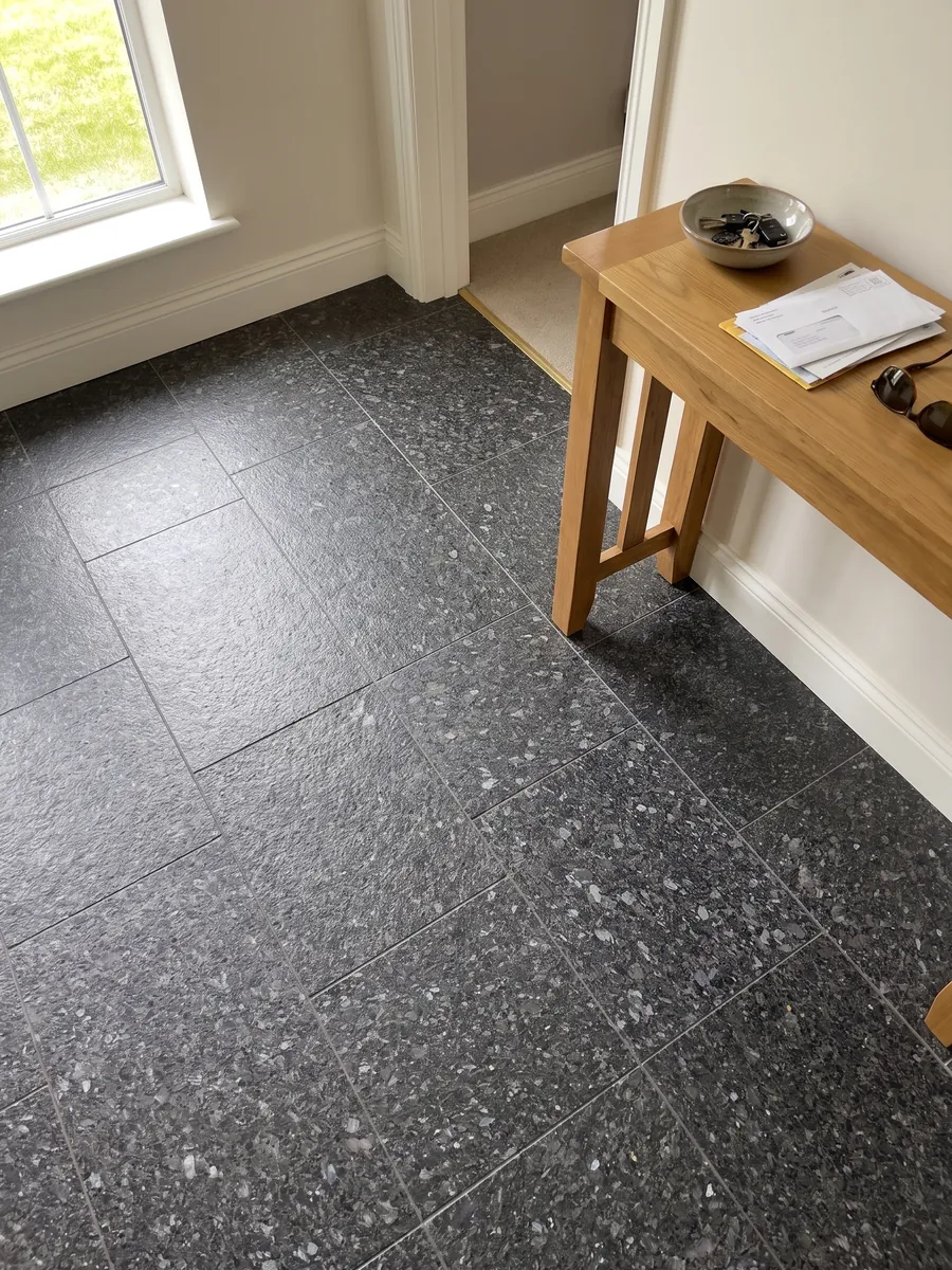 Entryway floor in large slabs of black Stargate granite in natural light: granular anthracite gray with gray and violet crystals