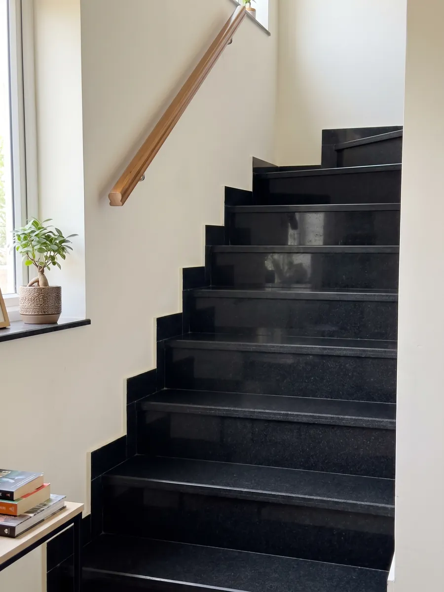 Interior staircase with Titanium Black granite treads and a handrail: an almost flat, uniform black with an extremely fine grain you only notice up close