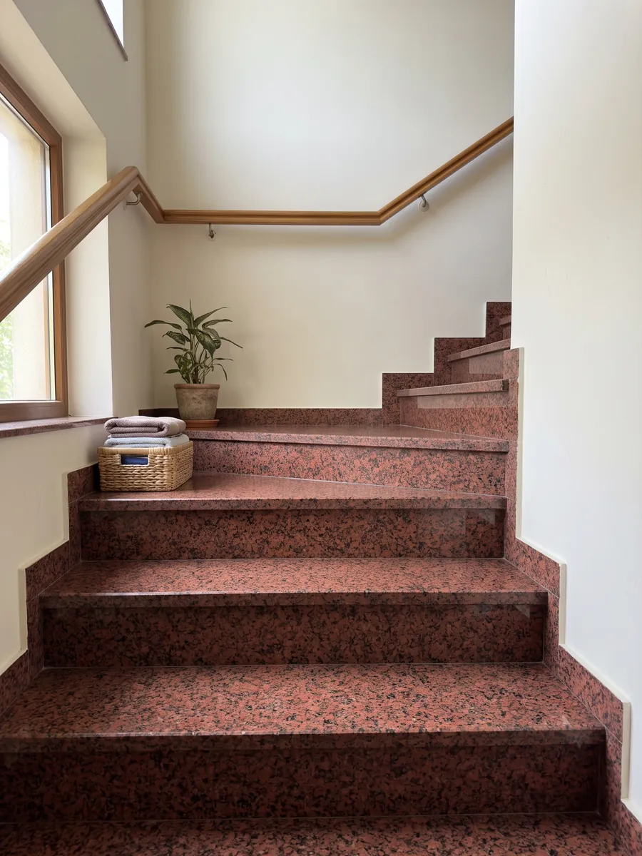 Interior staircase with red Balmoral Red granite treads and a handrail: deep granular red with black dots spread evenly