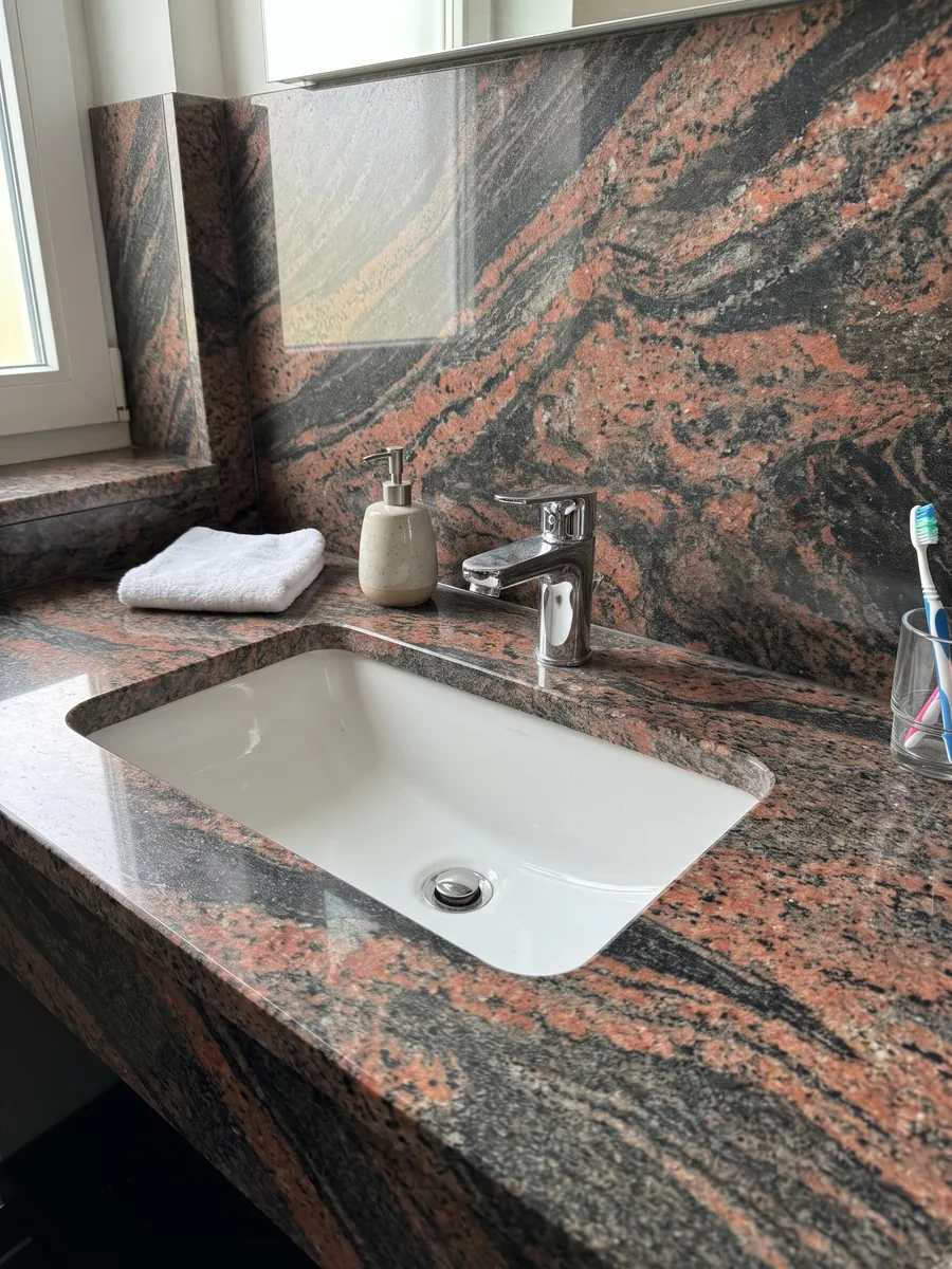 Bathroom vanity top and wall in Indian Aurora red granite with a white sink and chrome fixtures: coral and dark gray waves running diagonally