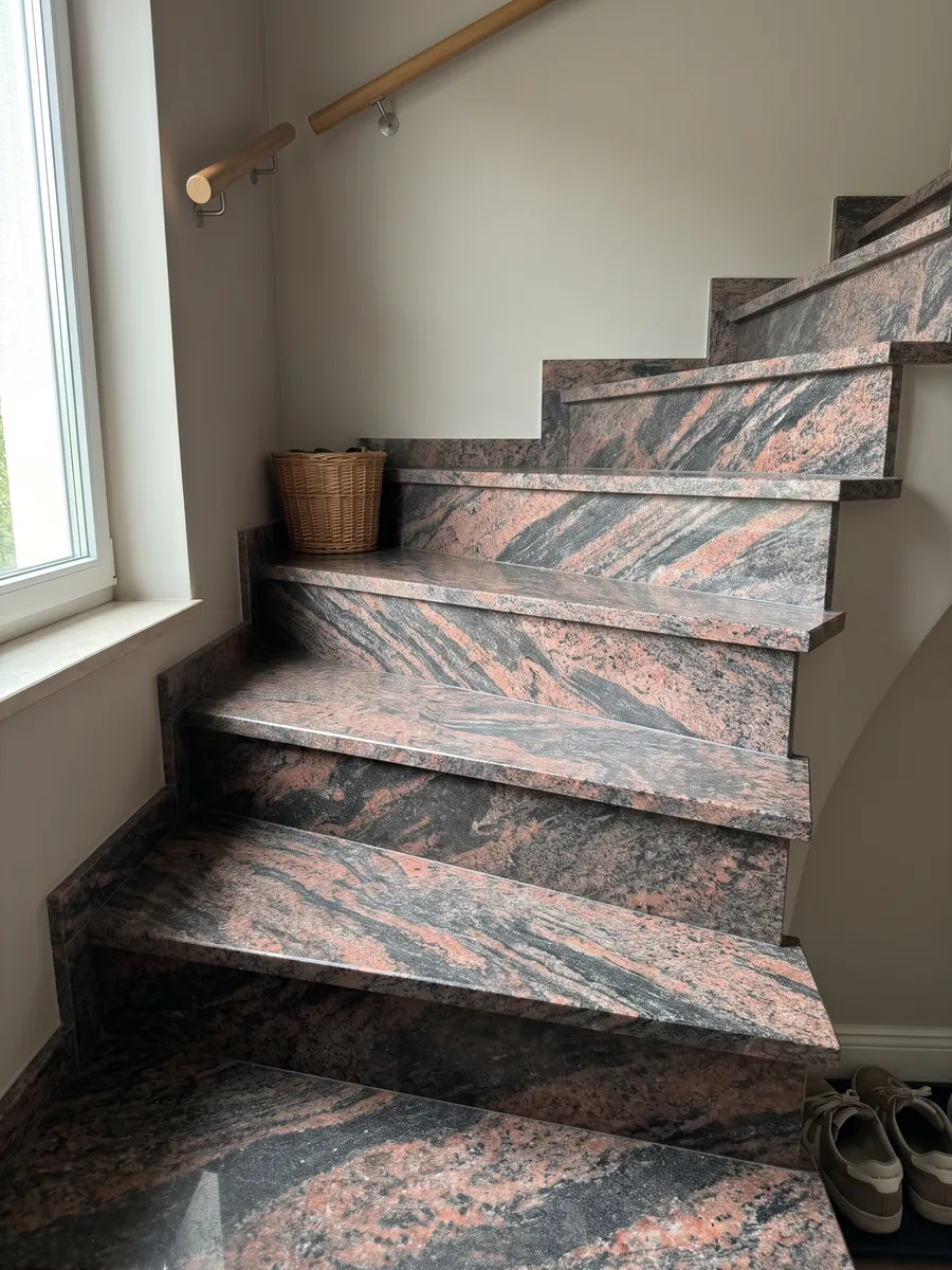 Indoor staircase with Indian Aurora red granite steps and a handrail: coral and dark gray waves running diagonally