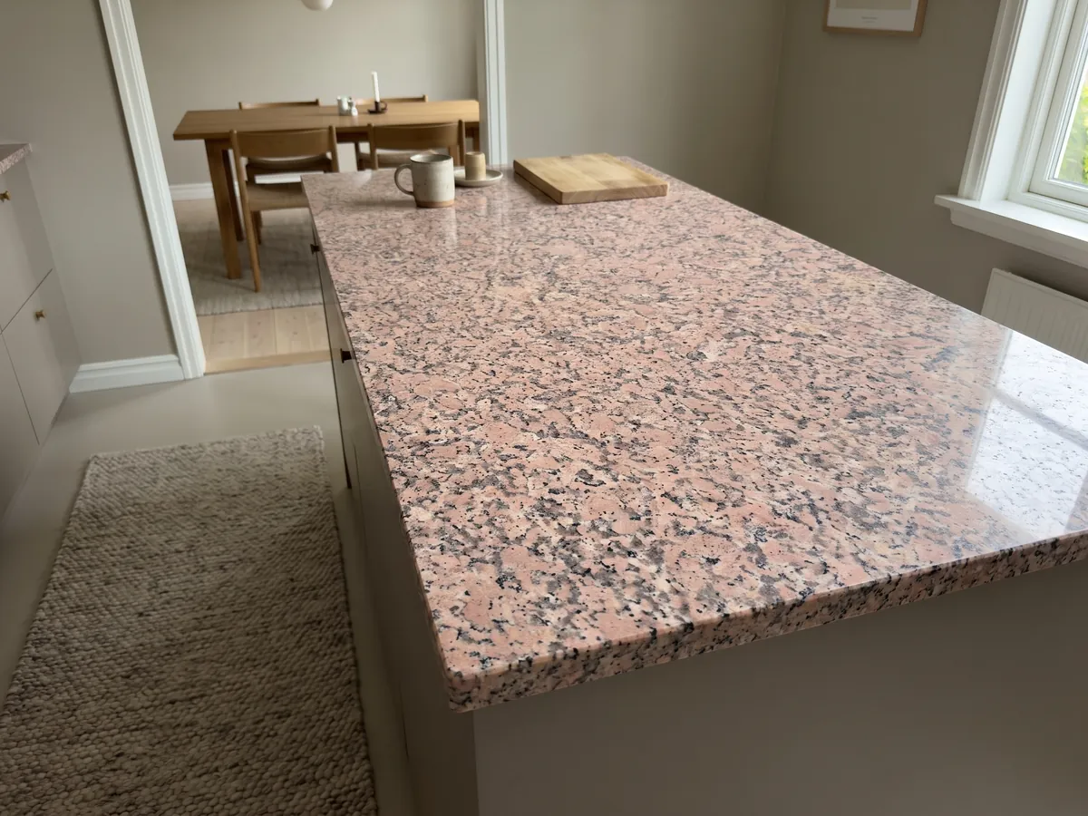 Kitchen island with a Rosa de Salto granite countertop and a straight edge in a kitchen with natural light: mottled pink with dark gray and white speckles