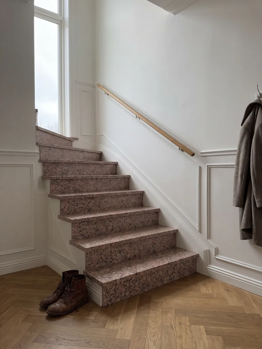 Interior staircase with Rosa de Salto granite steps and a handrail: mottled pink with dark gray and white speckles