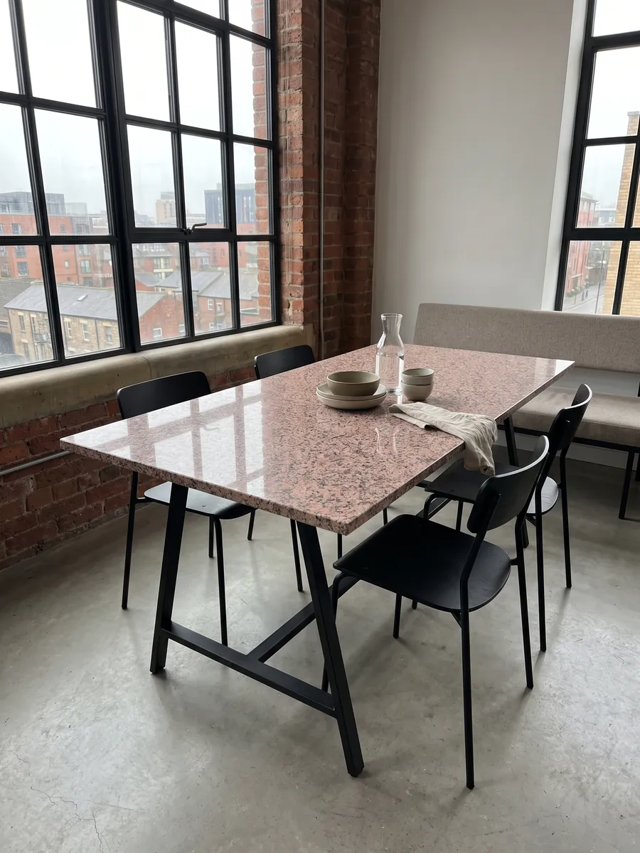 Dining table with a Rosa de Salto granite top on a steel base: mottled pink with dark gray and white speckles