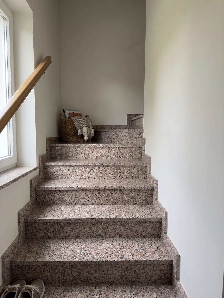 Interior staircase with pink Limbara granite treads and a handrail: pinkish-brown grain with white and black crystals