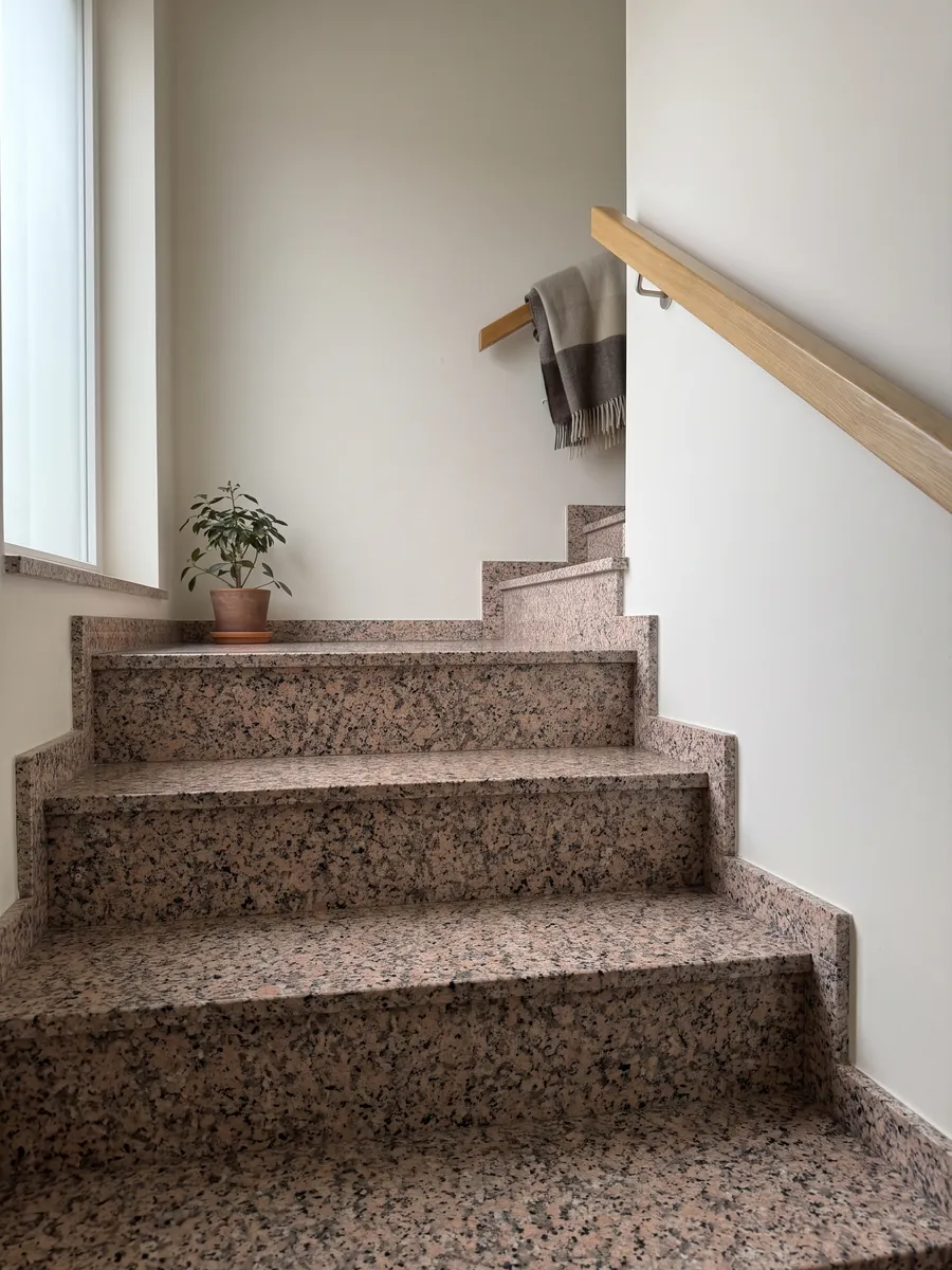 Interior staircase with Rosa Porriño granite steps and a handrail: speckled salmon pink with black specks